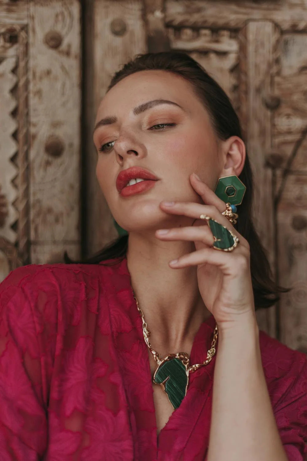 Woman in pink dress, wearing green earrings, necklace, and ring.